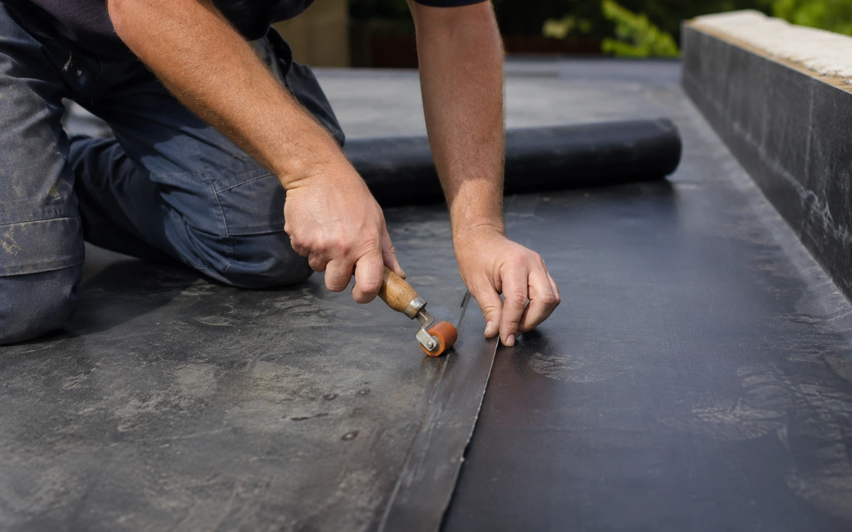 Roofing crew rolling out an EPDM rubber membrane on a low-slope roof